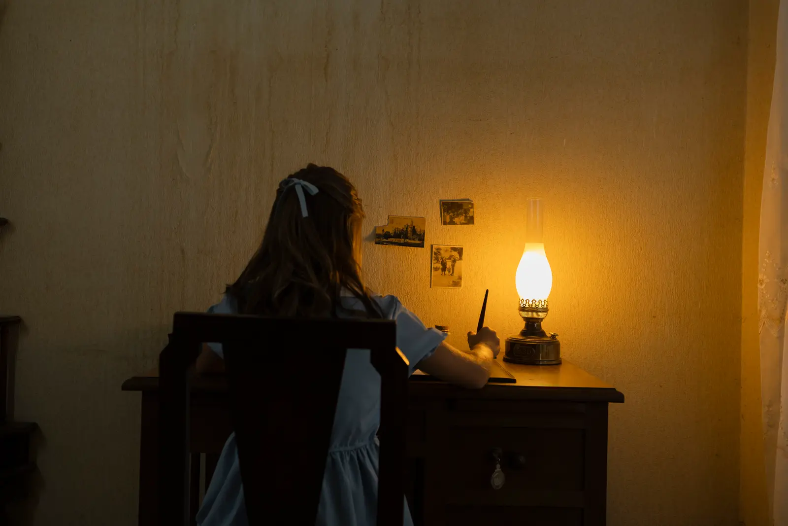 Una niña escribe una carta a la luz de un candil, escena del videoclip de «Queridos todos:»